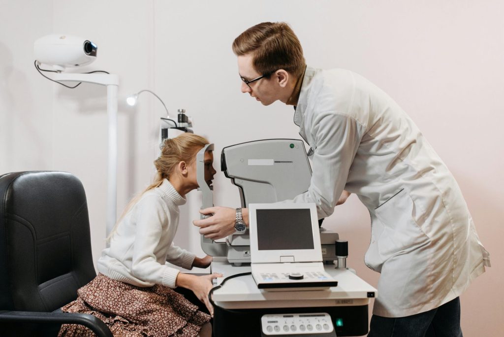 Young girl undergoing eye examination with optometrist using medical equipment in a clinic.