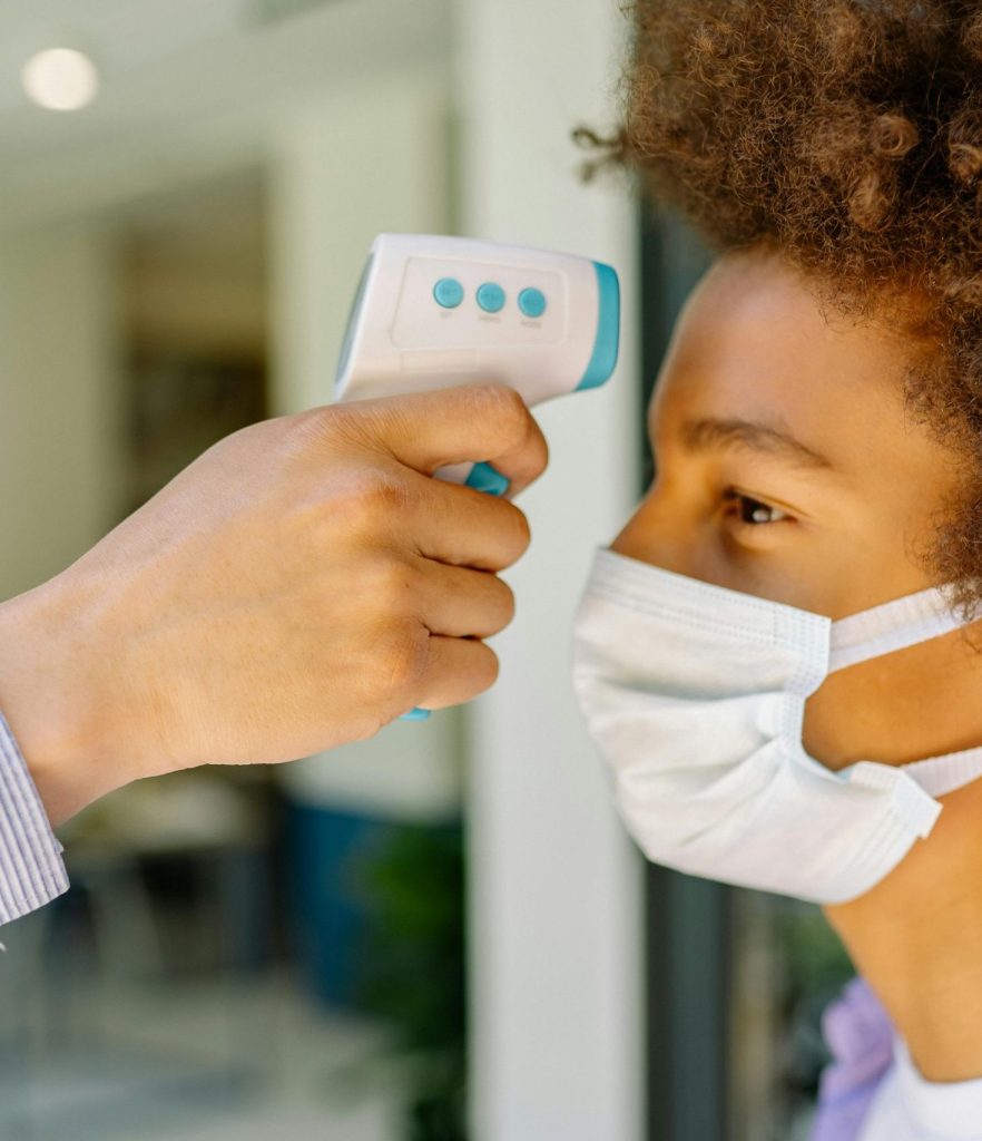 A young boy wearing a mask getting his temperature checked at school during COVID-19 pandemic.