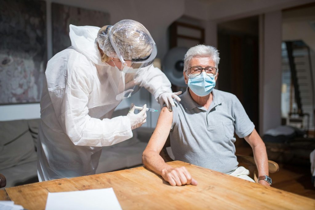 A healthcare worker administers a COVID-19 vaccine to an elderly man indoors, symbolizing health and safety.
